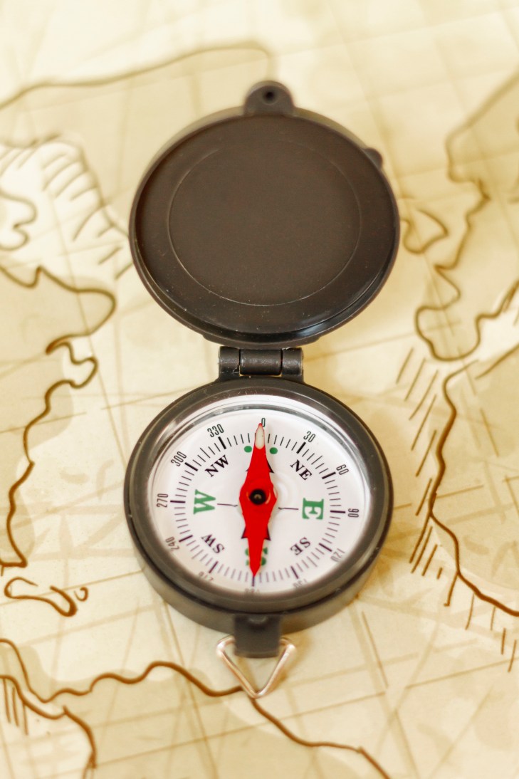 Open compass with a red needle pointing north, placed on a vintage map background.